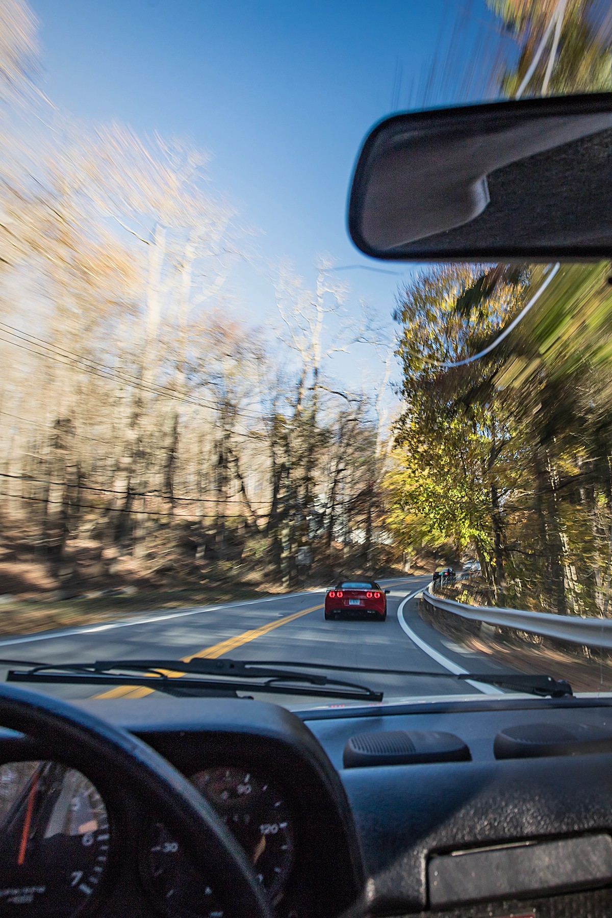 Driver's view through the windshield, following a coupe on an autumn road